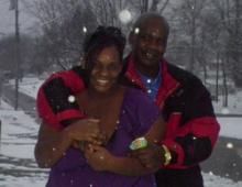 A photo of James and his wife outside, with their arms around each other, as snow falls around them